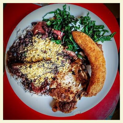 Una feijoada brasileña acompañada de banana empanada y un bistec de cerdo